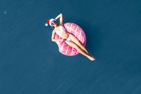 Young woman wearing Santa hat and bikini with inflatable ring in sea, top view. Christmas vacationの写真素材