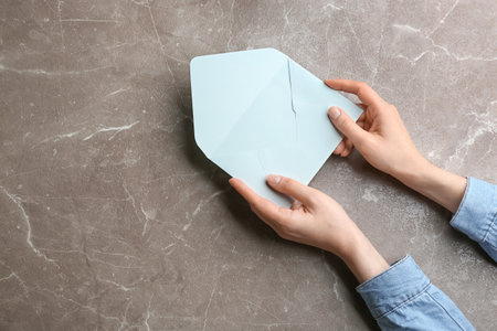 Woman holding paper envelope on marble background, closeup