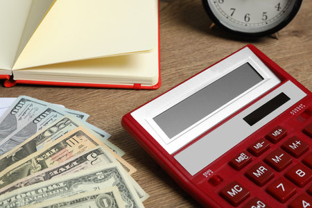 Calculator, notebook, money and alarm clock on wooden table, closeup. tax accounting