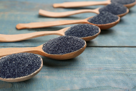 Poppy seeds in spoons on blue wooden table, closeupの写真素材