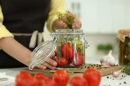 Woman putting dill into pickling jar at table in kitchen, closeupの写真素材