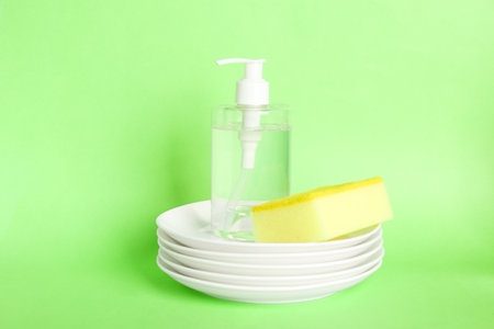 Detergent, plates and sponges on green background. clean dishes