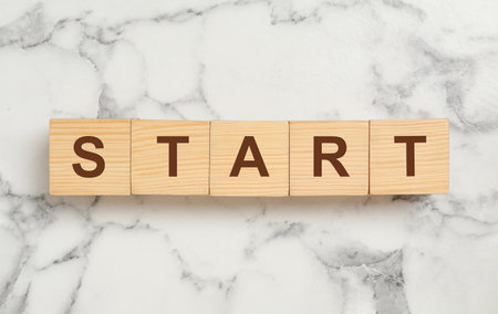 Word START made with wooden cubes on white marble background, flat layの写真素材