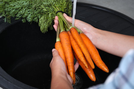 Woman washing ripe carrots with running water in sink, closeupの写真素材