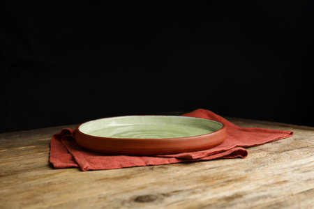 Empty plate and napkin on wooden table against black backgroundの写真素材