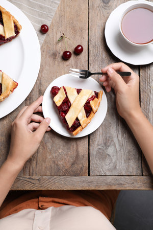 Woman eating delicious cherry pie on wooden table, top viewの写真素材