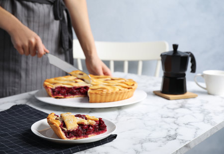 Closeup view of woman cutting tasty cherry pie at white marble table, focus on plate with sliceの写真素材