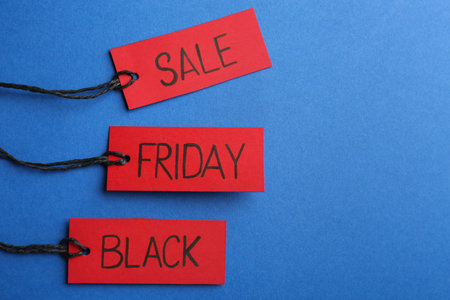 Red tags with words BLACK FRIDAY SALE on blue background, flat lay. Space for textの写真素材