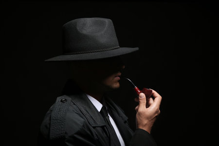 Old fashioned detective with smoking pipe on dark backgroundの写真素材