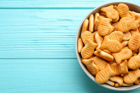 Delicious goldfish crackers in bowl on light blue wooden table, top view. Space for textの写真素材