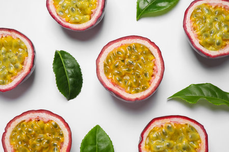 Halves of passion fruits (maracuyas) and green leaves on white background, flat layの写真素材