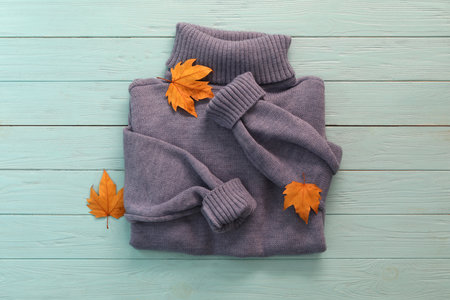 Warm sweater and dry leaves on blue wooden background, flat lay. autumn season