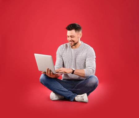Happy man with laptop on red backgroundの写真素材