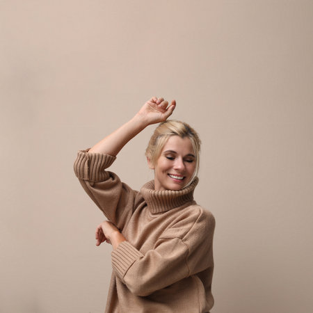 Happy woman in stylish sweater on beige backgroundの写真素材