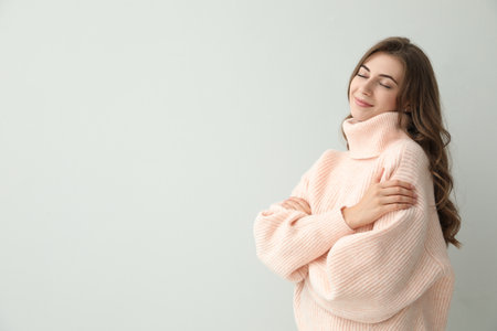 Beautiful young woman wearing warm pink sweater on light background. Space for textの写真素材