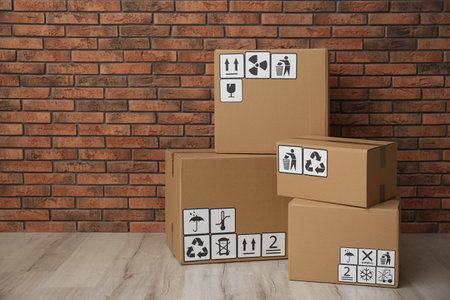 Cardboard boxes with different packaging symbols on floor near brick wall. Parcel delivery