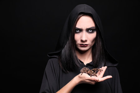 Mysterious witch with spooky spider on black background, space for textの写真素材