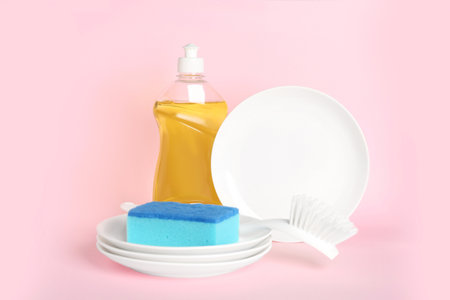 Detergent, plates and sponge on pink background. clean dishes