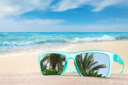 Palms mirroring in sunglasses on sandy beach near oceanの写真素材