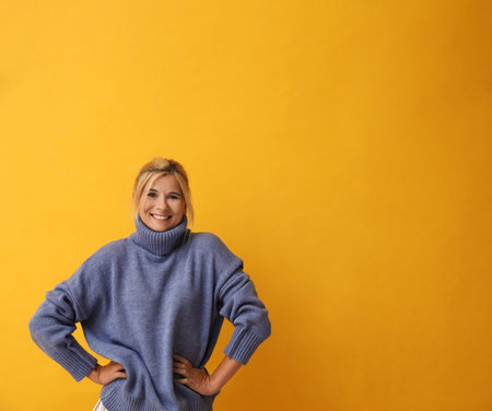 Happy woman in stylish sweater on yellow background. Space for textの写真素材