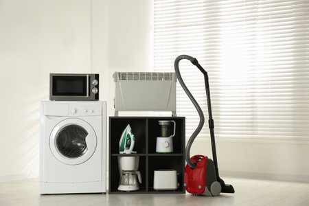 Modern vacuum cleaner and different household appliances near window indoorsの写真素材