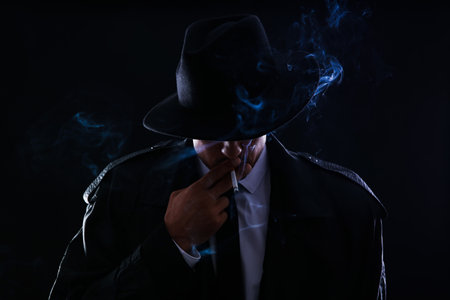 Old fashioned detective smoking cigarette on dark backgroundの写真素材
