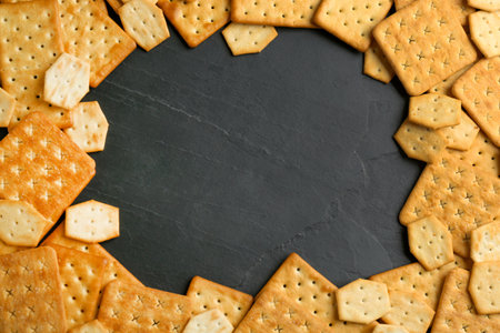 Frame of delicious crackers on black background, flat lay. Space for text