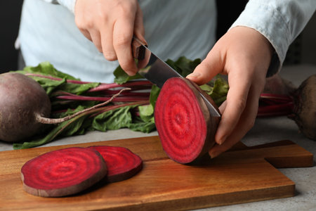 Woman cutting fresh red beet at table, closeup