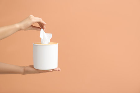 Woman taking paper tissue from holder on light brown background, closeup. Space for textの写真素材