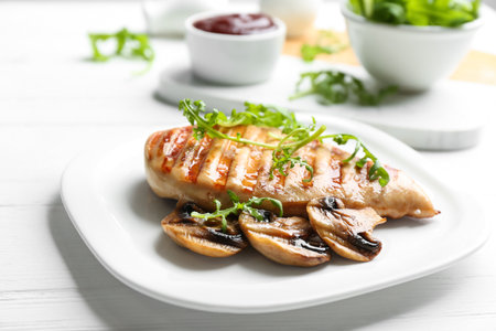 Tasty grilled chicken fillet with mushrooms and arugula on white table, closeupの写真素材