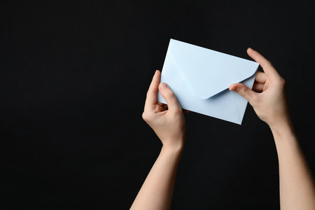 Woman holding white paper envelope on black background, closeup. Space for textの写真素材