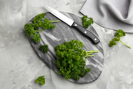 Fresh curly parsley, cutting board and knife on gray table, flat lay