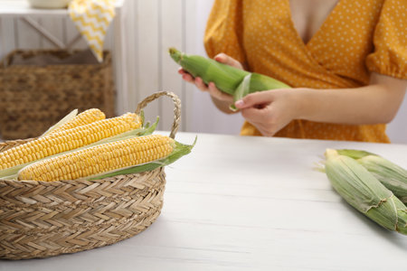 Woman husking corn cob at white wooden table, focus on basketの写真素材