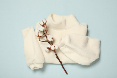 Warm sweater and cotton flowers on light blue background, flat lay. autumn seasonの写真素材
