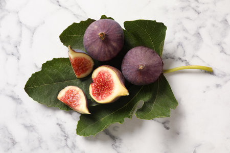 Whole and cut tasty fresh figs with green leaf on white marble table, flat layの写真素材