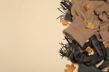 Flat lay composition with sweater and dry leaves on beige background, space for text. autumn season