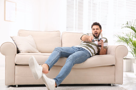 Lazy young man watching TV on sofa at home