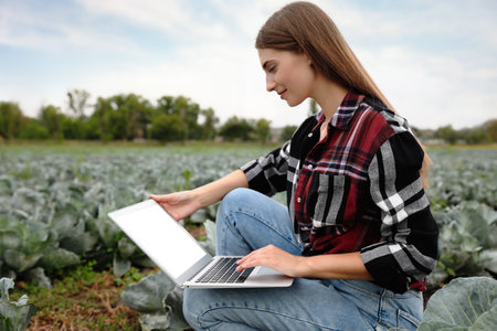 Woman using laptop with blank screen in field. agriculture technologyの写真素材