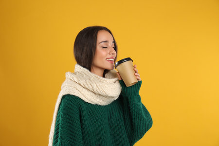 Happy beautiful woman with paper cup of mulled wine on yellow backgroundの写真素材