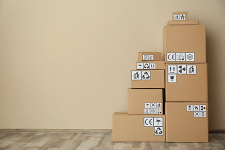 Cardboard boxes with different packaging symbols on floor near beige wall, space for text. Parcel deliveryの写真素材