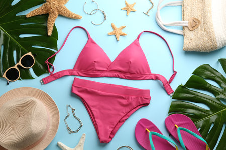 Beautiful pink bikini and beach accessories on light blue background, flat layの写真素材