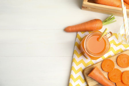 Freshly made carrot juice in mason jar on white table, flat lay. Space for textの写真素材