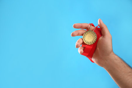 Man holding golden medal on light blue background, closeup. space for designの写真素材