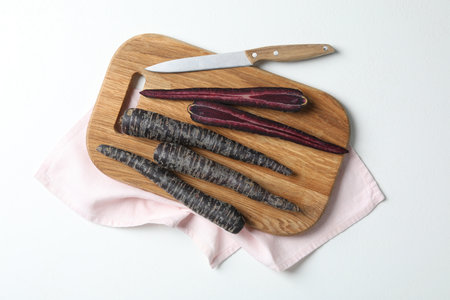 Raw black carrots, knife and cutting board on white table, flat layの写真素材