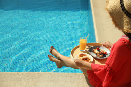 Young woman with delicious breakfast on tray near swimming pool, closeup. Space for textの写真素材