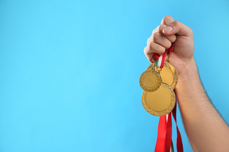 Man holding golden medals on light blue background, closeup. space for designの写真素材