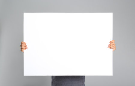 Man holding white blank poster on gray background. Mockup for designの写真素材