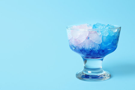 Shaving ice in glass dessert bowl on light blue background, closeup. Space for textの写真素材