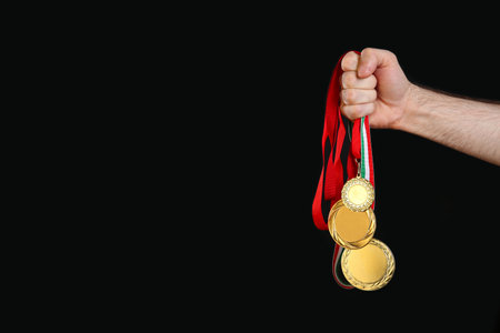 Man holding golden medals on black background, closeup. space for designの写真素材