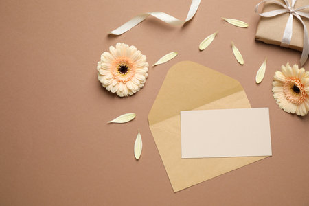 Beautiful herbera flowers, gift, envelope and blank card with space for text on brown background,...